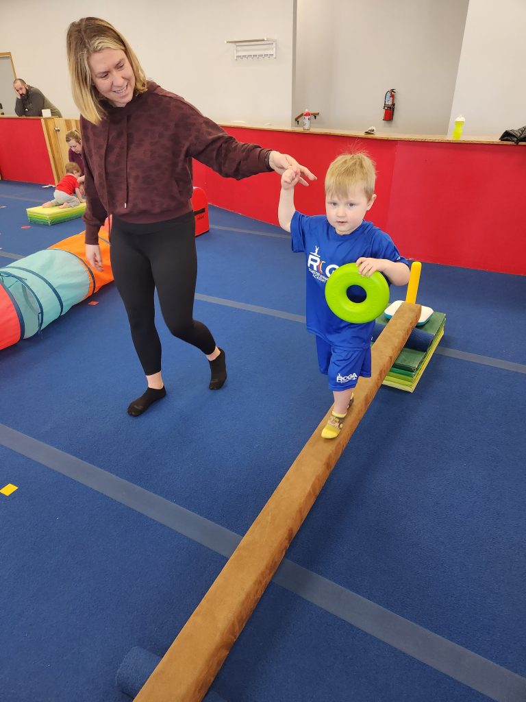 A child practicing on a balance beam with an adult's help
