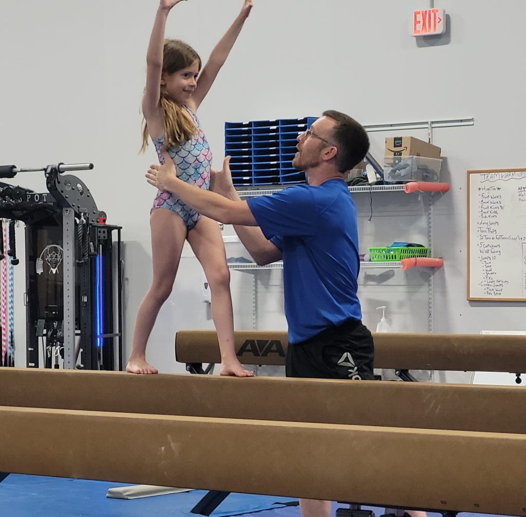 Girls practicing gymnastics with a coach's assistance