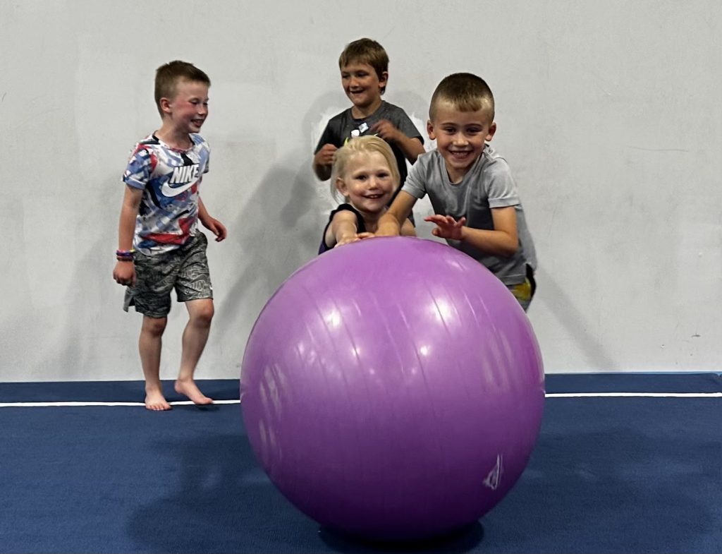 Three children with a large purple yoga ball at Kids Night Out