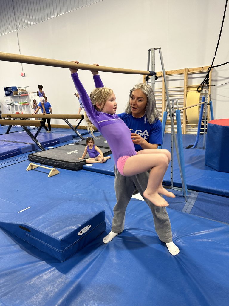 A girl practicing gymnastics movement with coach's help