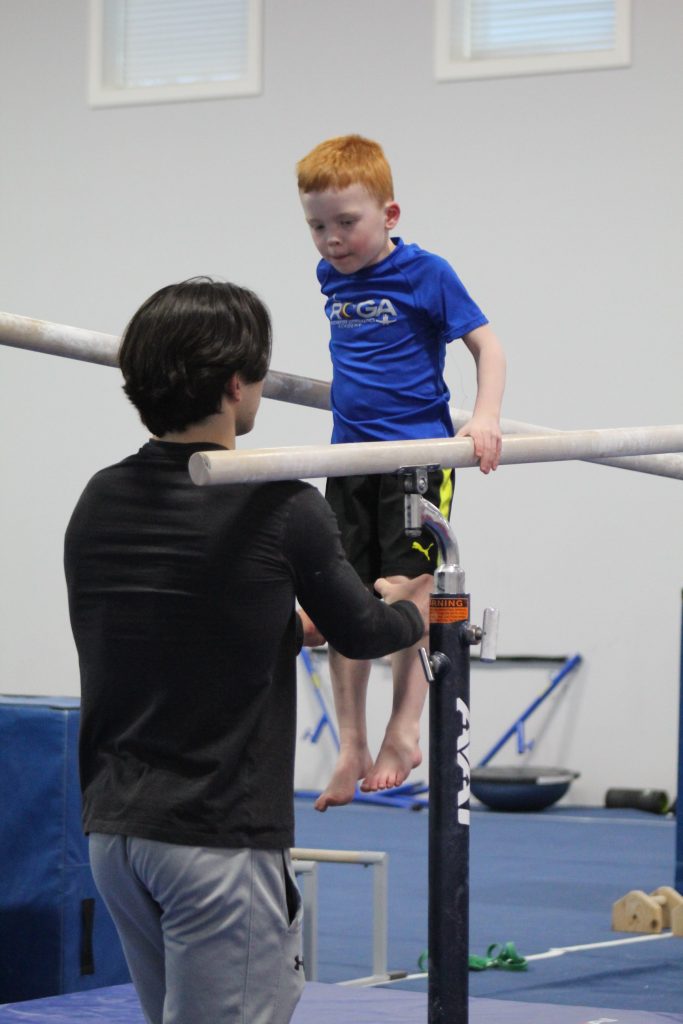 A boy practicing parallel bars with assistance