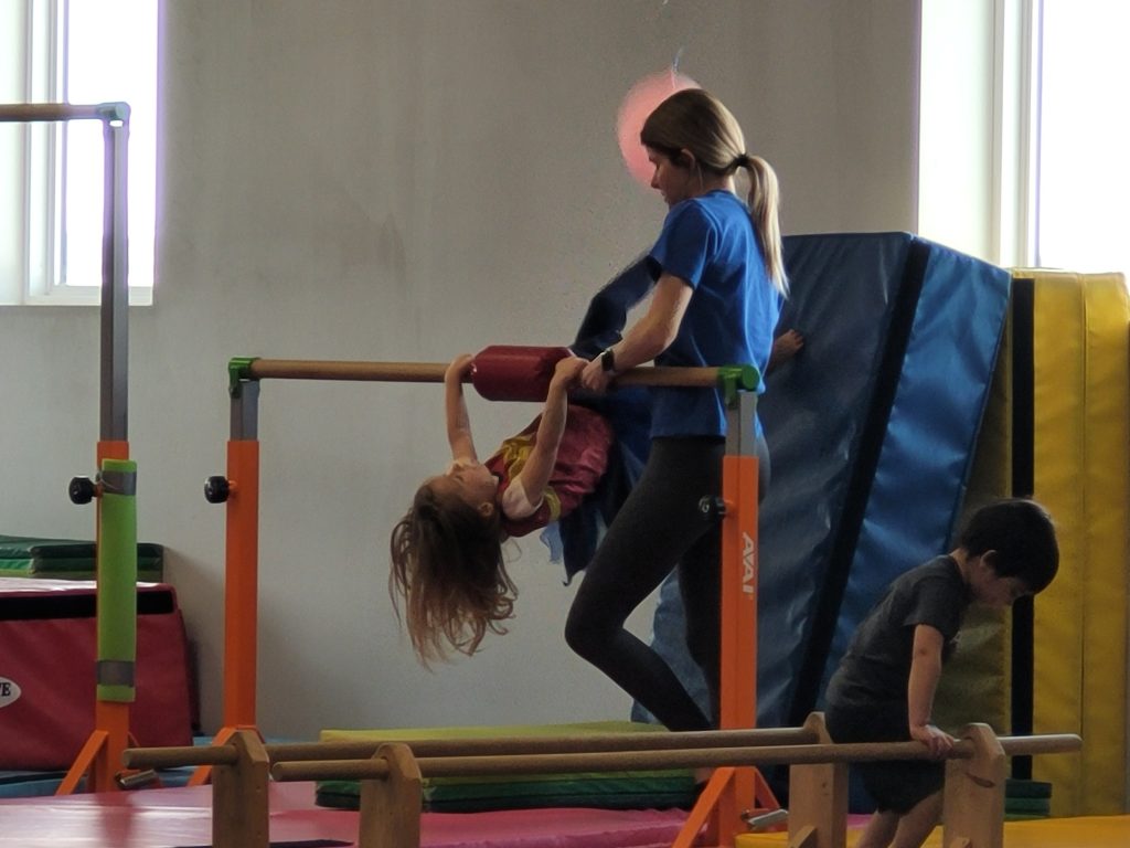 A preschool gymnast getting assistance from an instructor