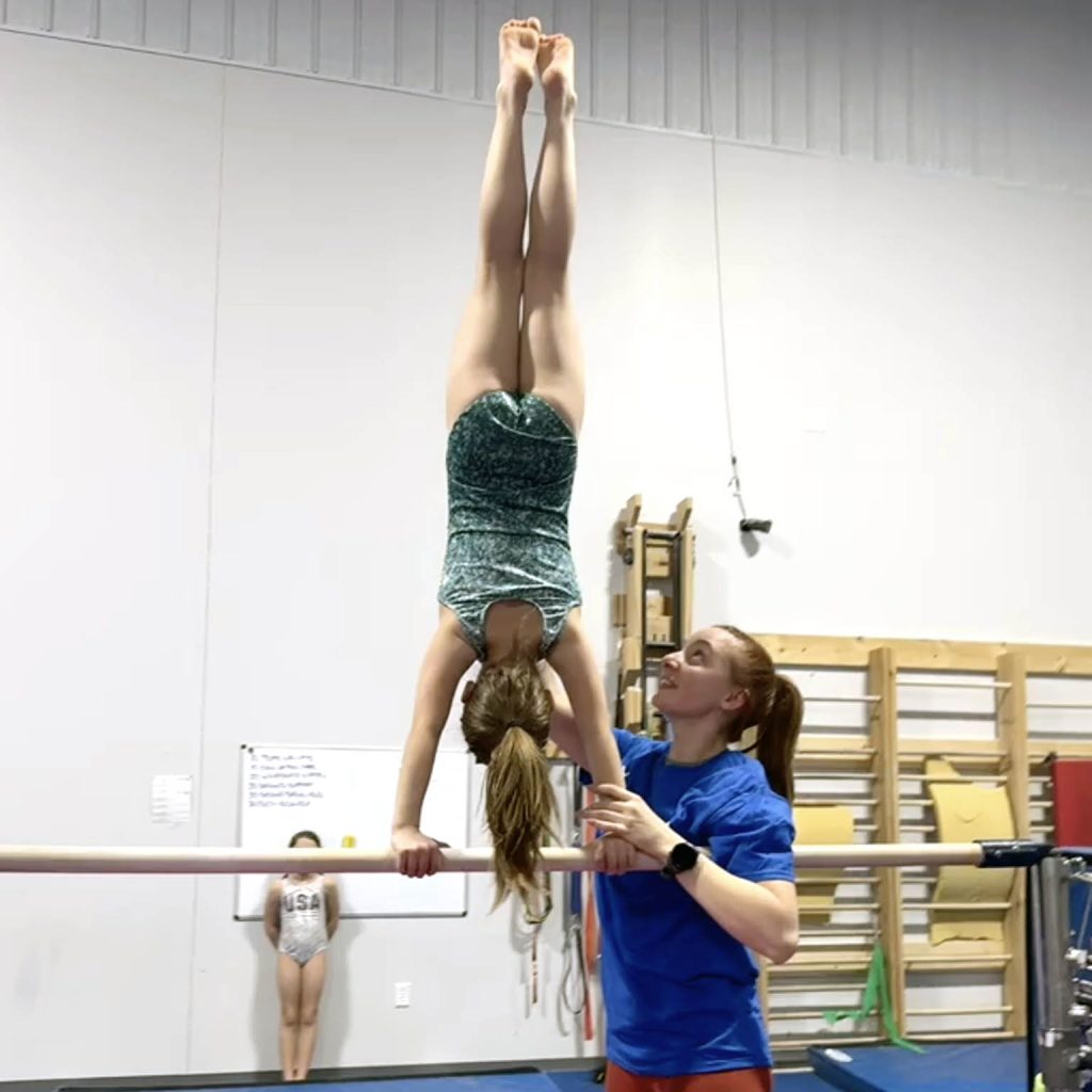 A girl gymnast practices a movement with the help of a coach