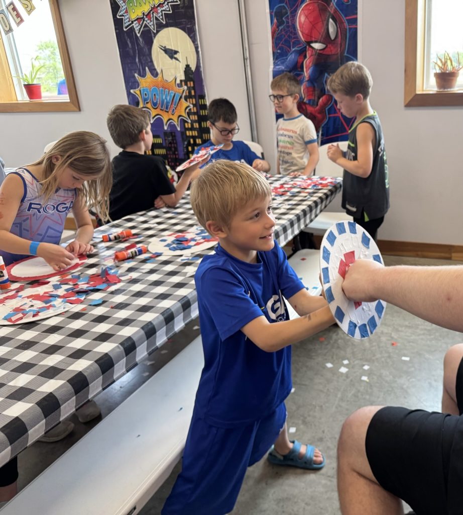 A boy playing with his superhero shield at the superhero-themed week of Camp ROGA